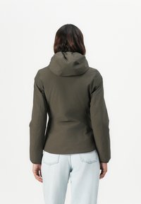 Olive green jacket with a hood, made of smooth, waterproof fabric. Fitted design, long sleeves, and elastic cuffs. Worn over light denim jeans.
