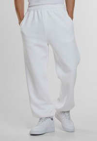 Witte katoenen joggingsbroek met een elastische tailleband, zijzakken en een ontspannen pasvorm, gecombineerd met witte sneakers. Soepele textuur.
