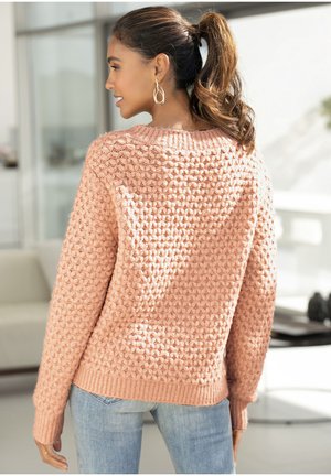 Strickpullover in Textur rosa mit lockerer Passform, geripptem Kragen und Bündchen, kombiniert mit hellblauen Jeans. Detailliertes, grob gestricktes Muster.