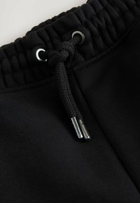 Schwarzer elastischer Bund mit geknotetem Zugband und metallischen Enden an schwarzem Stoff für Sweatpants.