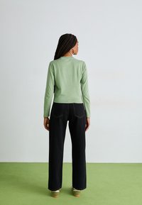 Μιντ πρ�άσινη μπλούζα με μακρύ μανίκι συνδυασμένη με ψηλόμεσα μαύρα παντελόνια σε φαρδιά γραμμή. Ξεχωριστή λεπτομέρεια ραφής και υφασμάτινη υφή.