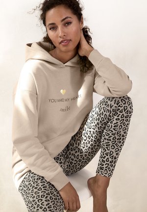 Beige Kapuzenpullover mit goldenem Herzdesign und dem Text "DU LÄSST MEIN HERZ lächeln", kombiniert mit Leggings im schwarz-grauen Leopardenmuster.
