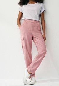 Roze linnen cargobroek met zijzakken en een losse pasvorm, gecombineerd met een lichtgrijze t-shirt en witte sneakers.