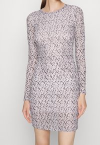 Długa sukienka z długimi rękawami o dopasowanym kroju, wykonana z lekkiego materiału, z powtarzającym się geometrycznym wzorem w jasnoróżowym i ciemnobrązowym kolorze.