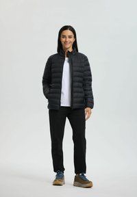 Sort puffjakke med standkrave, lynlås og vandret syninger. Bæres over en hvid skjorte og kombineres med sorte bukser og brune sko.