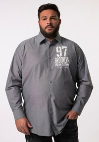 Camicia grigia a maniche lunghe con bottoni, con una trama minima. Presenta una stampa grafica frontale che include "97" e "BROOKLYN URBAN CLOTHING."