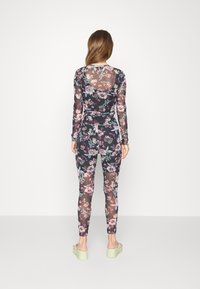 T-shirt de mangas longas em malha floral e leggings combinando em tons escuros, com um padrão botânico, textura transparente e design ajustado.