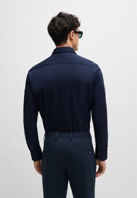 Navy long-sleeve shirt with a collar and buttoned cuffs, paired with matching pants featuring an elastic waistband and side pockets.