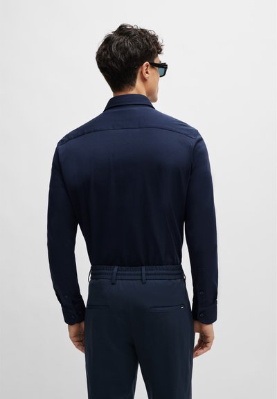 Chemise à manches longues bleu marine avec col et poignets à bouton, associée à un pantalon assorti avec une taille élastique et des poches latérales.