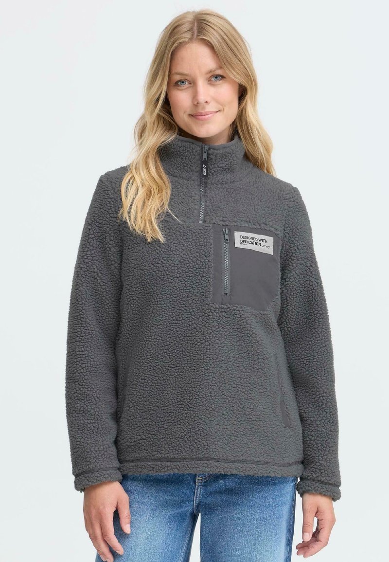 Tumehall fleece-pullover kõrge kaelusega, millel on tõmblukuga rinna-tasku ja tekstuurne kangas. Sisaldab pitsat koos ääristusega.