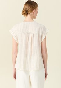 Blusa beige chiaro con maniche corte arrotolate, caratterizzata da righe verticali multicolori e un design con retro arricciato. Tessuto texturizzato.