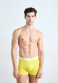 Yellow cotton boxer shorts featuring a white waistband with "NIKE" logo. The shorts have a fitted design with a smooth texture.