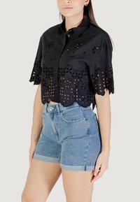 Cropped shirt nera con design floreale a occhio di pernice, maniche corte e orlo scallop, abbinata a pantaloni shorts in denim a vita alta, azzurri.