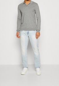 Maglietta polo grigia a maniche lunghe con colletto, abbinata a jeans azzurri chiari e sneaker bianche. Il tessuto sembra morbido e texturizzato.