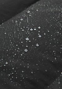 Tessuto nero con una superficie liscia, caratterizzato da numerose gocce d'acqua che si sono accumulate in superficie, indicando resistenza all'acqua.