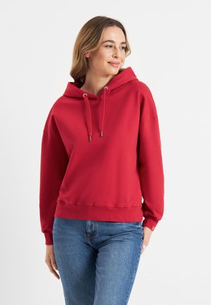 Rode hoodie met verstelbare trekkoorden, ribgebreide manchetten en zoom. Gladde stoftextuur. Gecombineerd met blauwe spijkerbroek.