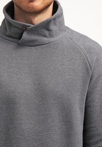 Harmaa neule, jossa on korkeakauluksinen malli, napitusyksityiskohta ja tekstuuriset olkasaumat. Pehmeä, neulotusta kankaasta valmistettu, sileäpintainen.