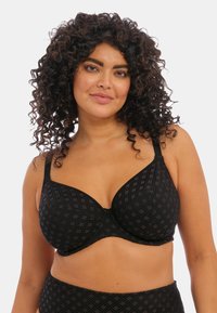 Soutien-gorge noir avec un design texturé mettant en avant de petits motifs géométriques. Il possède des bretelles réglables et des baleines pour le soutien.