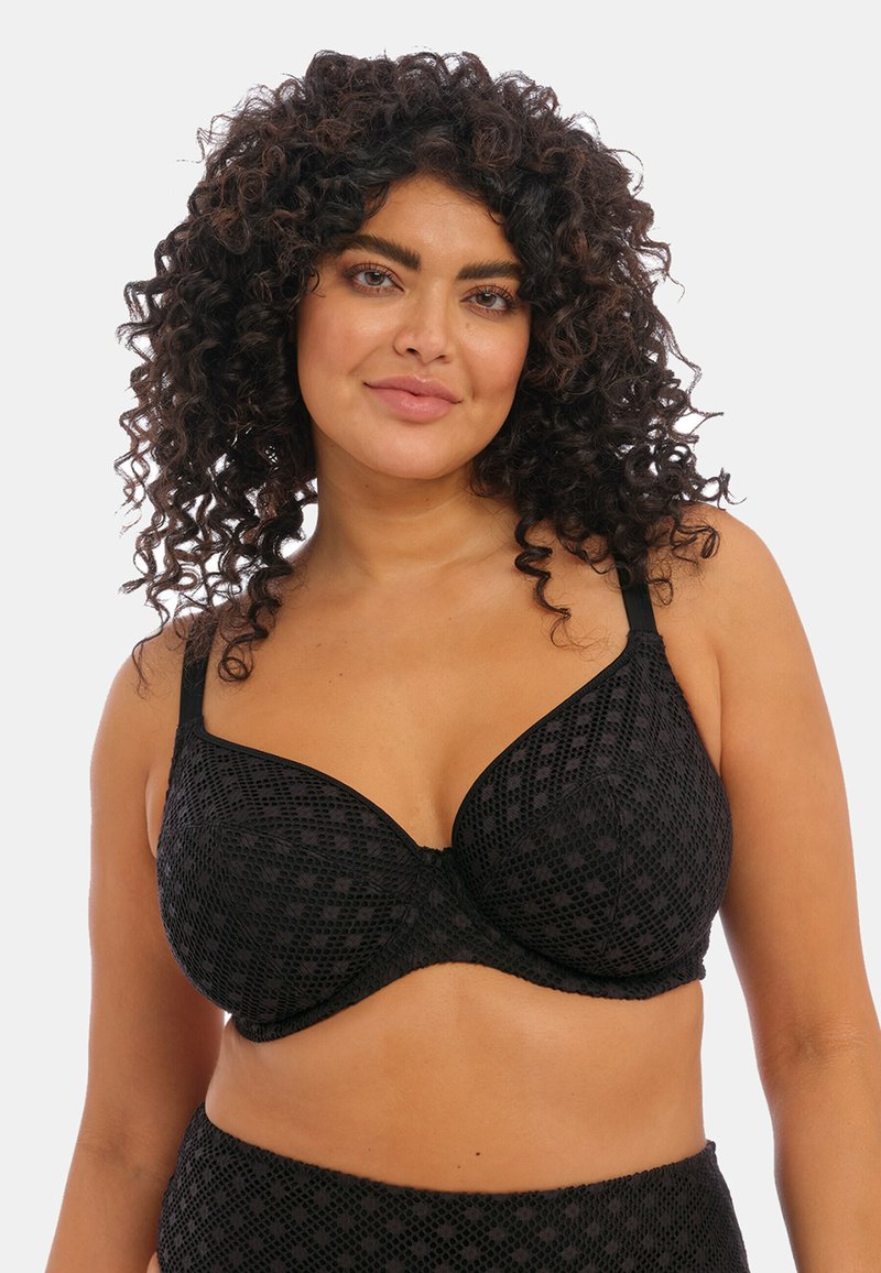 Soutien-gorge noir avec un design texturé mettant en avant de petits motifs géométriques. Il possède des bretelles réglables et des baleines pour le soutien.