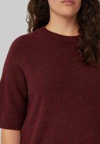 Burgunderfarbener Strickpullover mit kurzen Ärmeln und einem gerippten Rundhalsausschnitt. Weiche Textur mit einem subtilen Muster und einer lässigen Passform, ausgestattet mit Raglanärmeln.