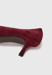 Scarpa con tacco alto in suede borgogna con punta affusolata e tacco di 7 cm a cono. Texture liscia con rifinitura opaca. Design minimalista, senza hardware visibile.