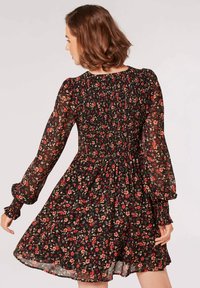Schwarzes Blumenkleid mit langen, durchsichtigen Ärmeln, gerafftem Oberteil und schwingendem Rock. Es hat ein rotes und grünes Blumenmuster auf einem dunklen Hintergrund.