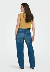 Kortärmad senapsgul topp utan ärmar i texturerad tyg, som kombineras med lösa blå denimjeans med två bakfickor och en mid-rise passform.