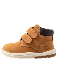 Tan suede boot with two velcro straps, brown leather accent at the top, white rubber sole with light brown tread, and logo on the side.