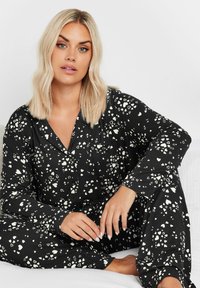 Conjunto de pijama negro con estampado de corazones blancos, que incluye una camisa de botones, mangas largas y pantalones a juego, fabricado en tejido suave.