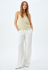 Camisola di un verde chiaro con texture e spalline sottili, abbinata a pantaloni bianchi a gamba larga, che evidenziano una vestibilità rilassata e un tessuto morbido.