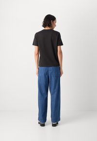 T-shirt nera a maniche corte con scollatura rotonda, abbinata a jeans blu a gamba larga con tasca posteriore e cuciture visibili.