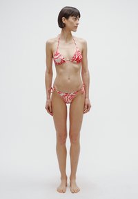Punase ja valge mustriga bikini, millel on kolmnurkne ülaosa ja külgedelt nööriga seotud alaosa, esitades siledat kangast kergelt tekstuuriga.