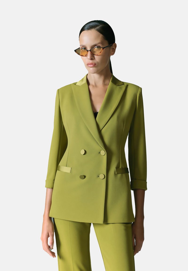 Blazer su misura verde oliva con design doppiopetto, revers a punta e due tasche frontali. Tessuto liscio, maniche a trequarti.