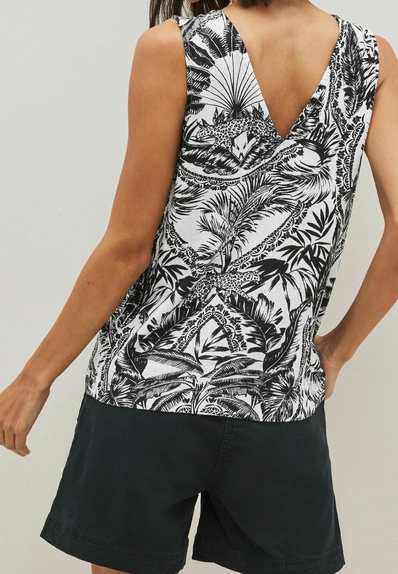 Haut sans manches noir et blanc à motifs avec feuilles tropicales et animaux, porté avec un short noir, vu de dos.