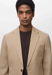 Bežna srajčna jakna s slim fit krojem, z notch reverji, z enim gumbom in žepom na prsih, prelečena preko temno rjave pletene puloverja.