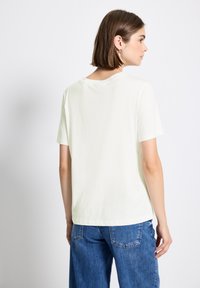 T-shirt vert clair à manches courtes avec une coupe décontractée, un col rond et une texture lisse. Associé à un jean en denim bleu ample.