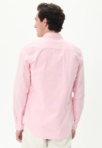Camicia a maniche lunghe, rosa, con bottoni realizzata in cotone. Presenta un colletto a punta, polsini con bottoni e un orlo curvo. Texture semplice senza fantasie.