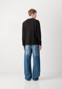 Zwarte lange mouwen shirt van ribstof, gecombineerd met oversized blauwe jeans met een lichte wassing en achterzakken, gezien vanaf de achterkant.