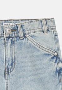 Vaqueros de mezclilla azul claro con un patrón desteñido, diseño de cinco bolsillos, cierre con botón metálico y detalles de costura en color canela. Etiqueta de la marca visible en el interior.