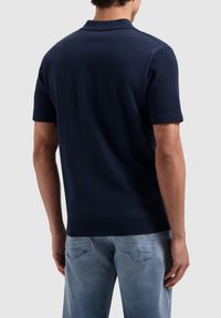 Navyblauwe gebreide polo met korte mouwen, geribbelde kraag en manchetten en een gestructureerde achterkant. Gekoeld met lichtblauwe spijkerbroeken.