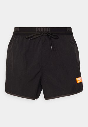 Bañador negro hecho de material ligero, con cintura ajustable mediante cordón, logo de PUMA en naranja y un diseño sencillo.