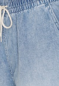 Ljusblå denimjoggers med elastisk midja, justerbar dragsko och sidfickor. Tyget har en mjuk, texturerad yta.