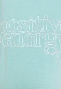 T-shirt azul claro feito de algodão suave, com texto branco que diz "energia positiva" em uma fonte divertida. Design de manga curta.
