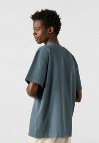 T-shirt a manica corta dal taglio rilassato, in blu ardesia, realizzato in cotone, con colletto rotondo e texture liscia. La vista posteriore mostra cuciture distintive.