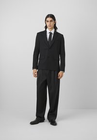 Black suit with a single button closure, notch lapels, two front pockets, and wide-leg trousers, paired with a white shirt and black tie.