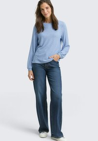Helles blaues Langarmoberteil mit geometrischem Muster, kombiniert mit weit geschnittenen Jeans. Das Outfit zeichnet sich durch eine lässige Passform und einen weichen Stoff aus.