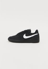 Sort sneaker med hvid Nike swoosh, snørebåndsdesign, tekstureret stofoverdel og gummisål. Lavprofil silhuet.