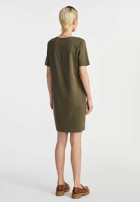 Oliwkowa sukienka do kolan z krótkimi rękawami, prostym okrągłym dekoltem i miękkiego materiału. Noszona z brązowymi butami na platformie, zatrzymując prosty design.