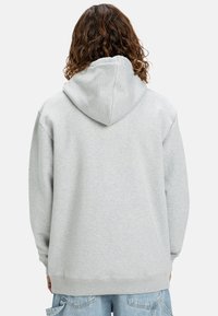 Sudadera con capucha gris de corte relajado, que cuenta con una gran capucha y puños acanalados. Textura suave, diseño minimalista, sin logos visibles.
