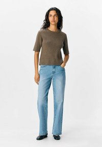 Maglione corto a maniche corte marrone a coste abbinato a jeans denim a gamba dritta blu chiaro e scarpe nere piatte. Sfondo semplice.